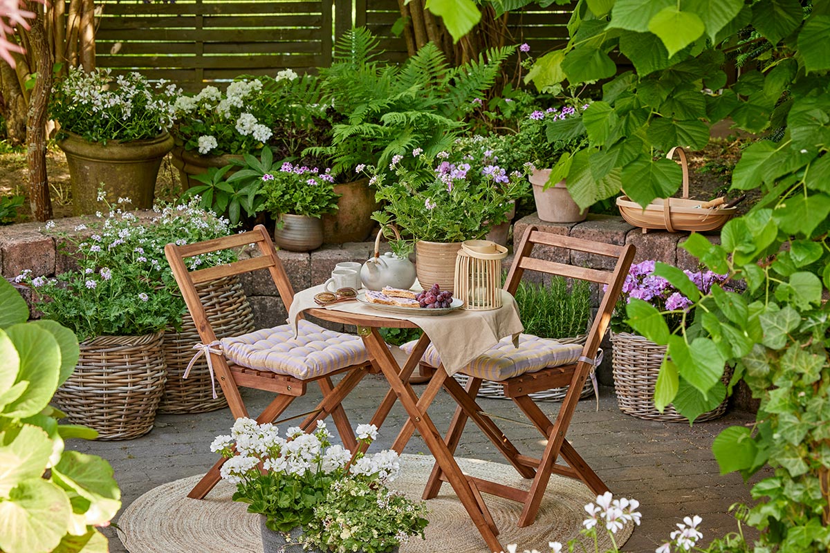 Acogedor rincón de jardín con mesa redonda, sillas de madera y plantas en macetas alrededor