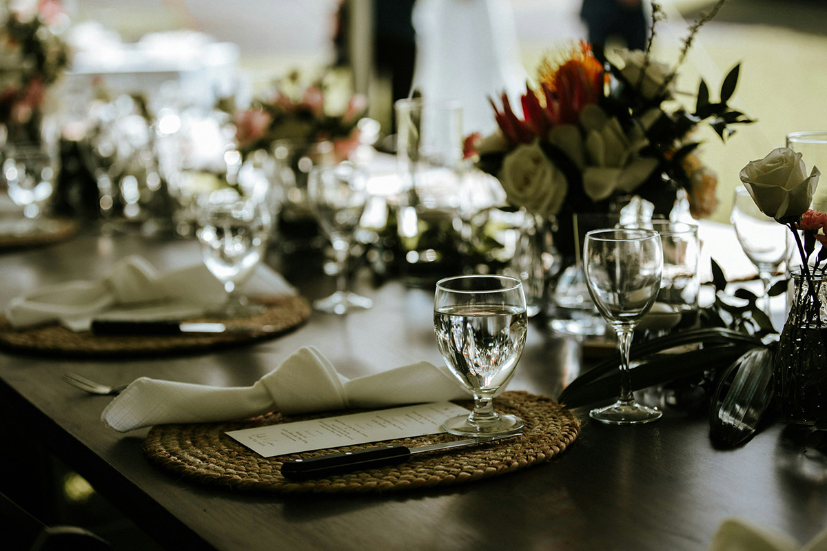 Mesa elegantemente decorada con copas, flores frescas y menús individuales para un evento formal