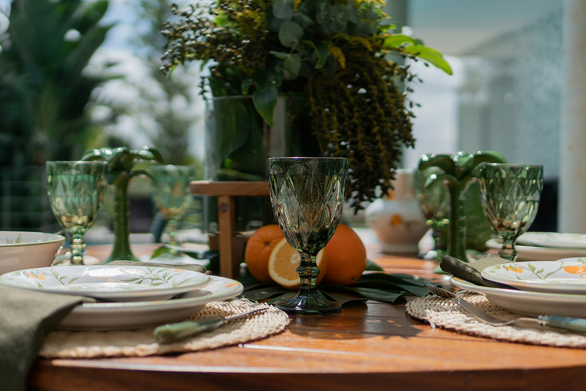 Mesa exterior con vajilla decorativa, copas verdes y centro de mesa con naranjas y follaje